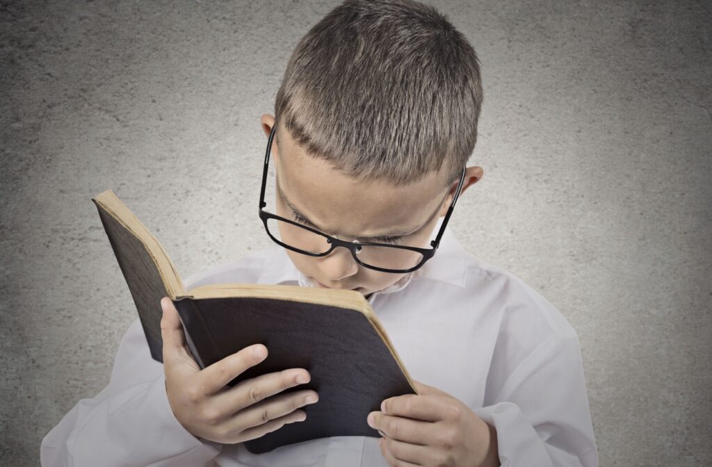 A young boy struggling to focus and holding a book close to his face.