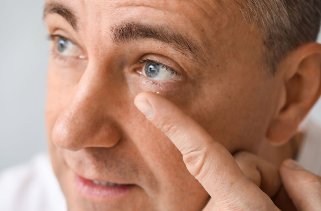 A close-up of a patient with a contact lens on the tip of his pointer finger as he tries to insert it in his eye.