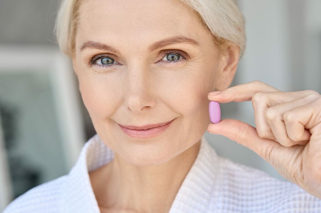 A close-up image of an older adult smiling while holding up a small pink vitamin that can help with macular degeneration.