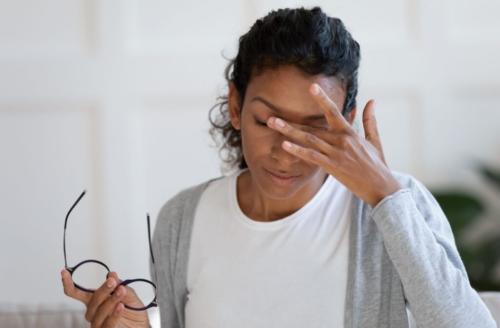 A person takes off their new glasses, closes their eyes in discomfort, and rubs the space between them