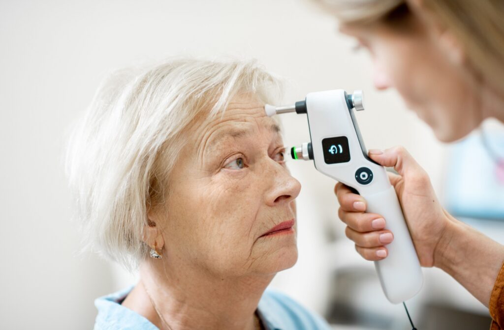Female eye care professional using handheld device to measure eye pressure of older senior woman.