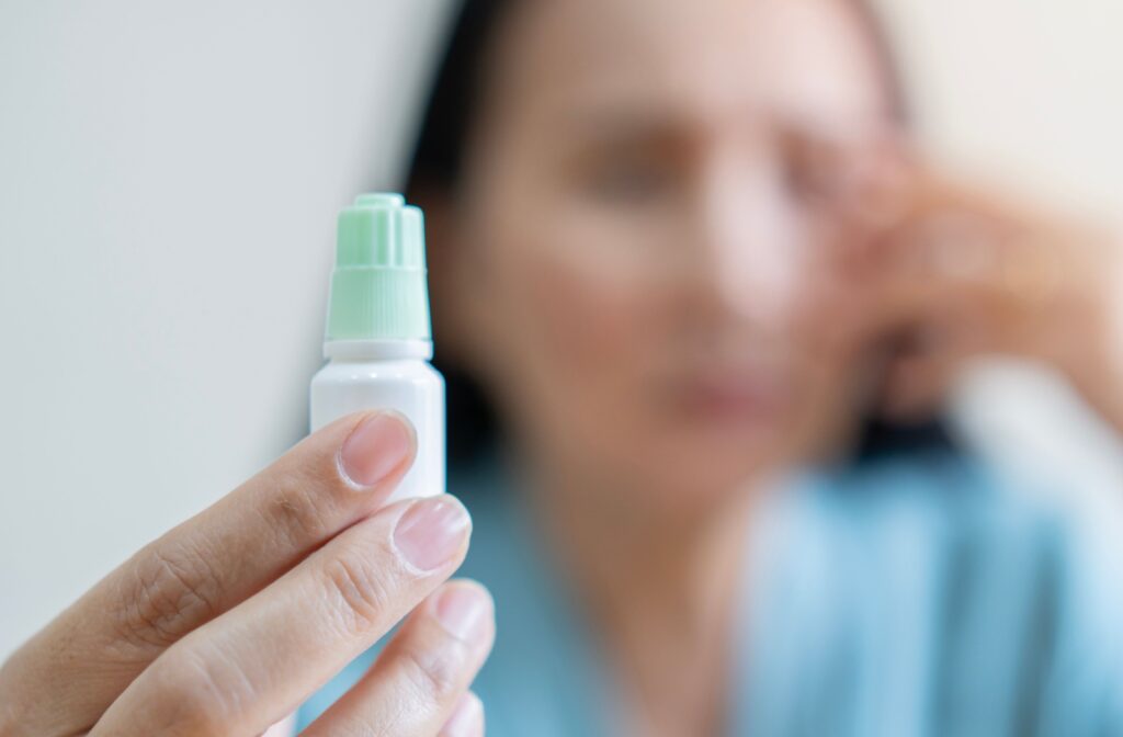 A person holding out a bottle of eye drops for pink eye, while they remained out of focus in the background.