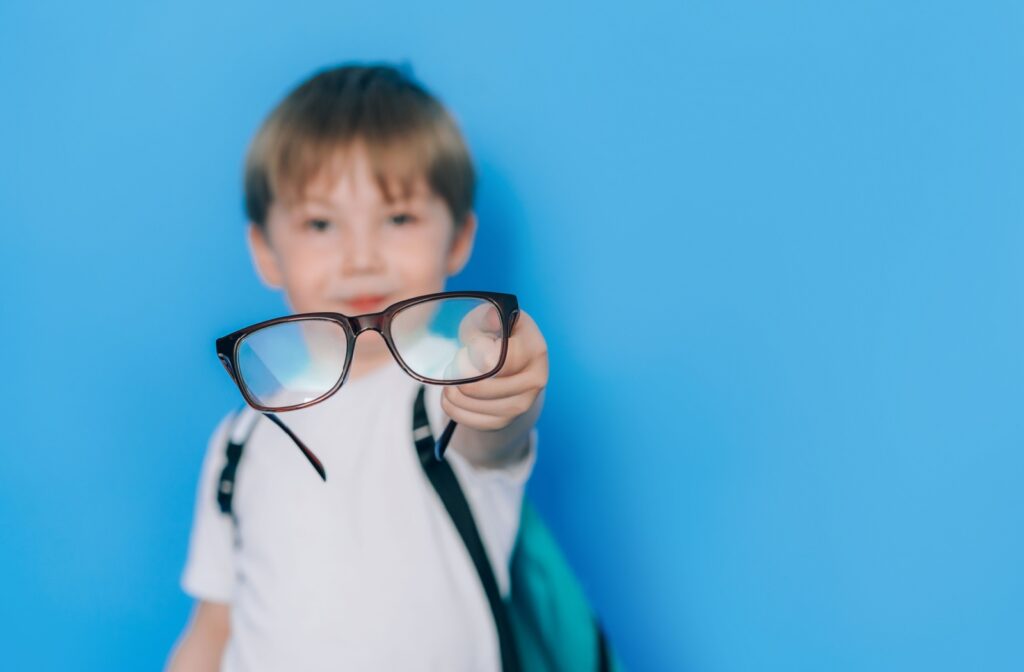 A young child wearing a backpack, holding a pair of glasses out in front of him that help to correct myopia.