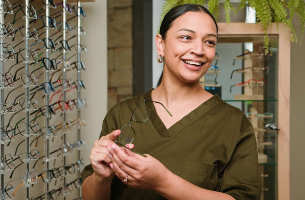 A smiling optician holding a pair of glasses from the eyewear display area in an optometry office.