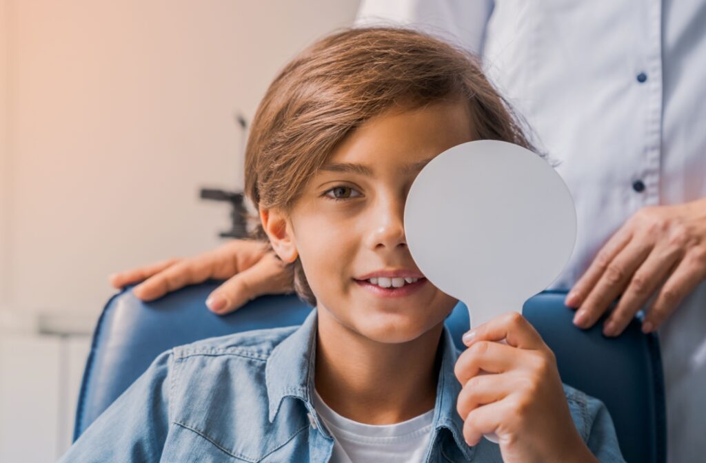 A young child at an eye exam with a cover over one eye, reading the letters on an eye chart to determine if they have myopia.