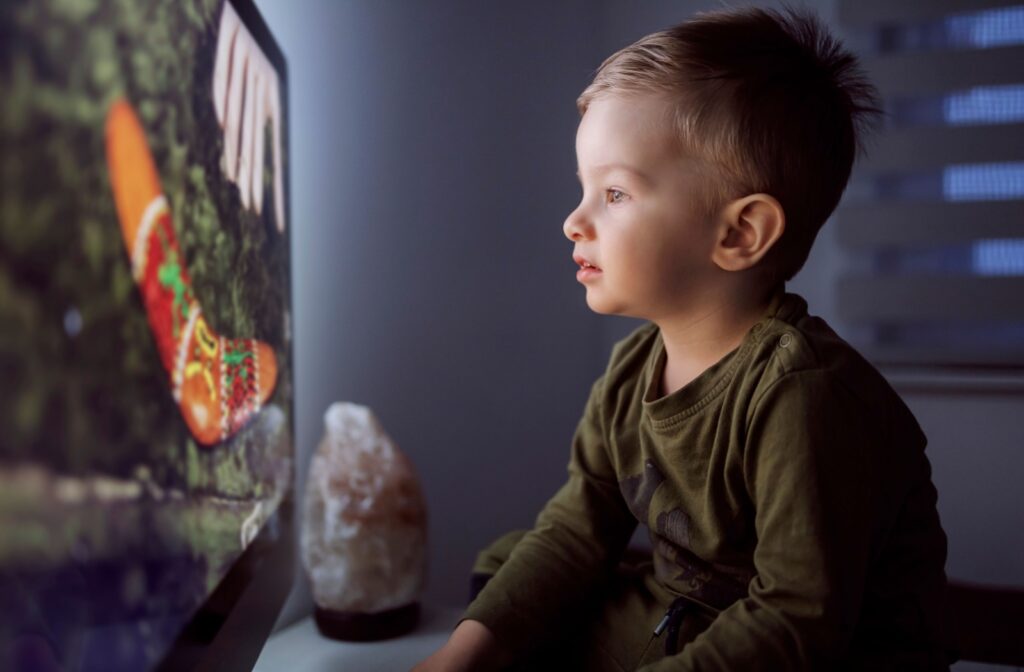 A young child sitting close to the TV to see the screen, which is a sign of myopia.